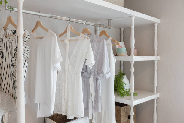 White summer dresses and tops hanging on a wooden rack in an organized closet, showcasing wardrobe additions.